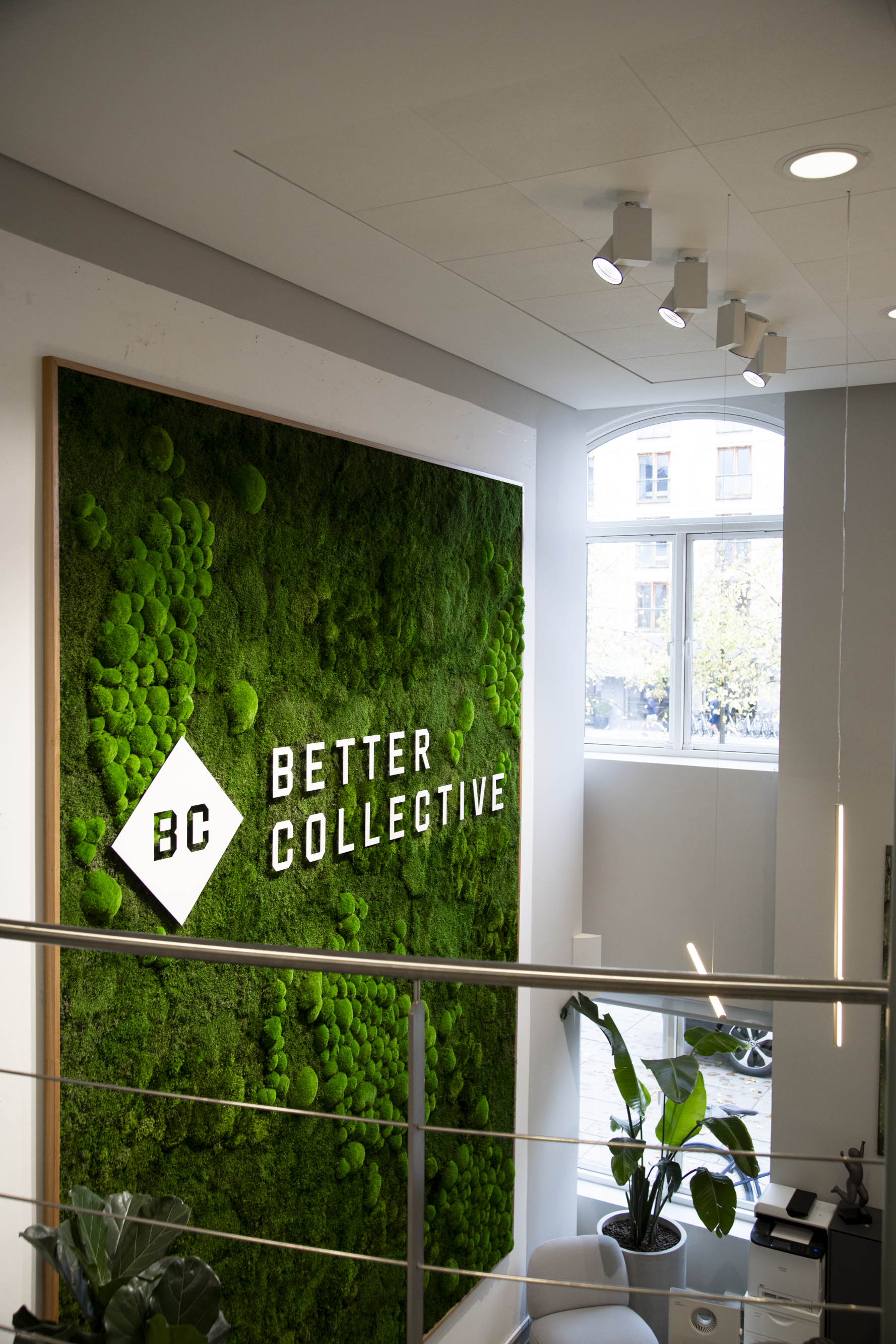 Indgangsområde med stor grøn mosvæg og Better Collective‑logo i et lyst og moderne kontormiljø.