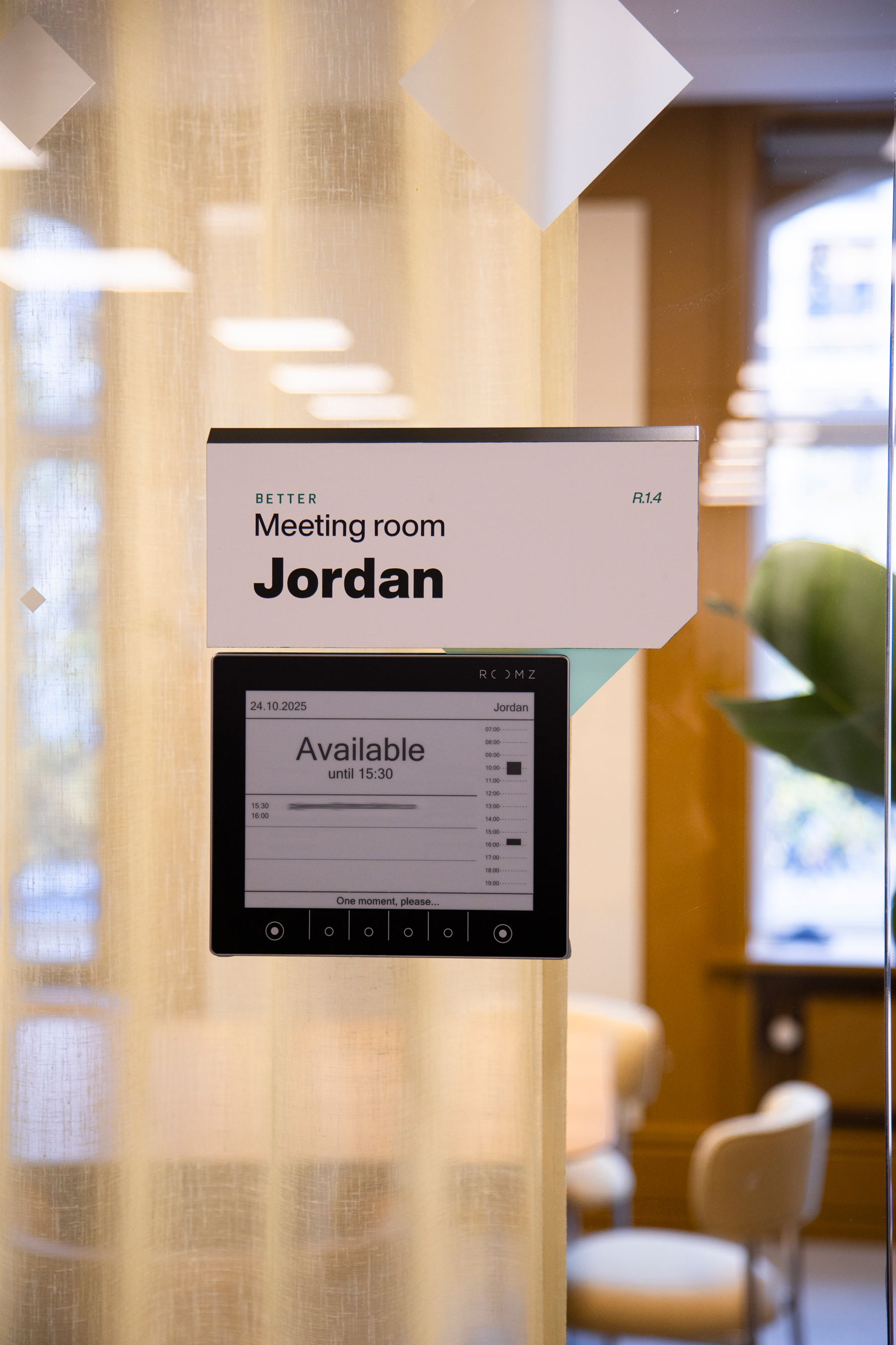Glasmødelokale med skiltet ‘Jordan’ og digital møderumsdisplay i et moderne kontormiljø.