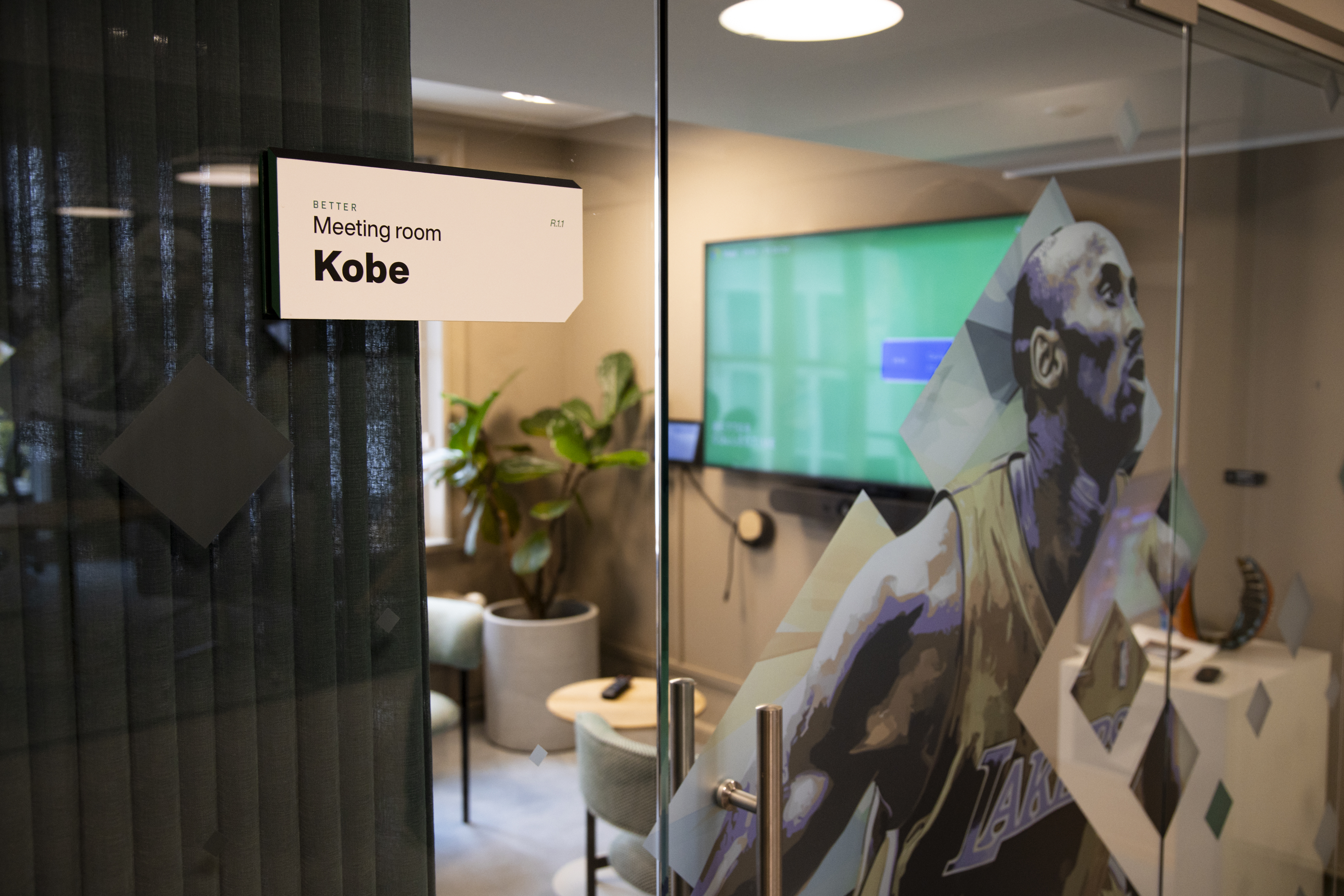 Glass‑fronted meeting room named ‘Kobe’, featuring sports‑themed artwork and modern interior design.