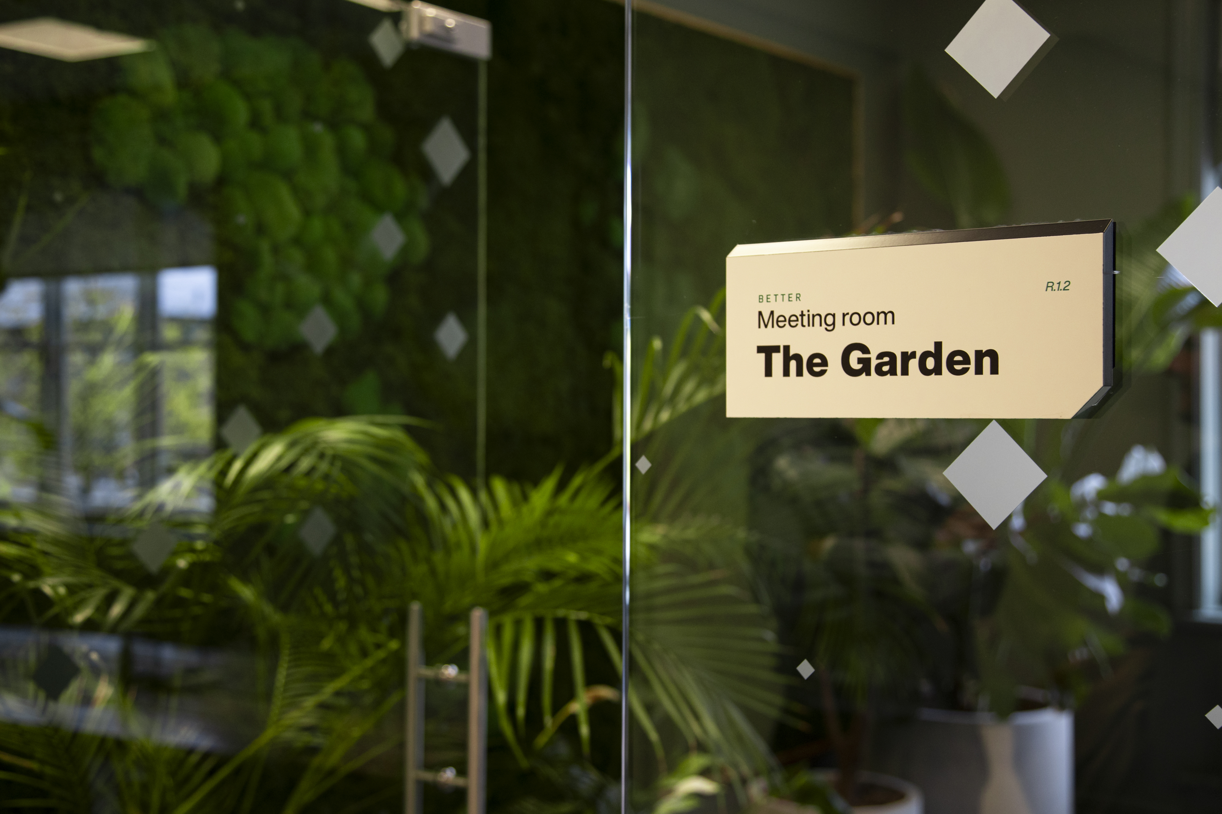 Glass‑fronted meeting room named ‘The Garden’, featuring lush greenery and modern interior design.