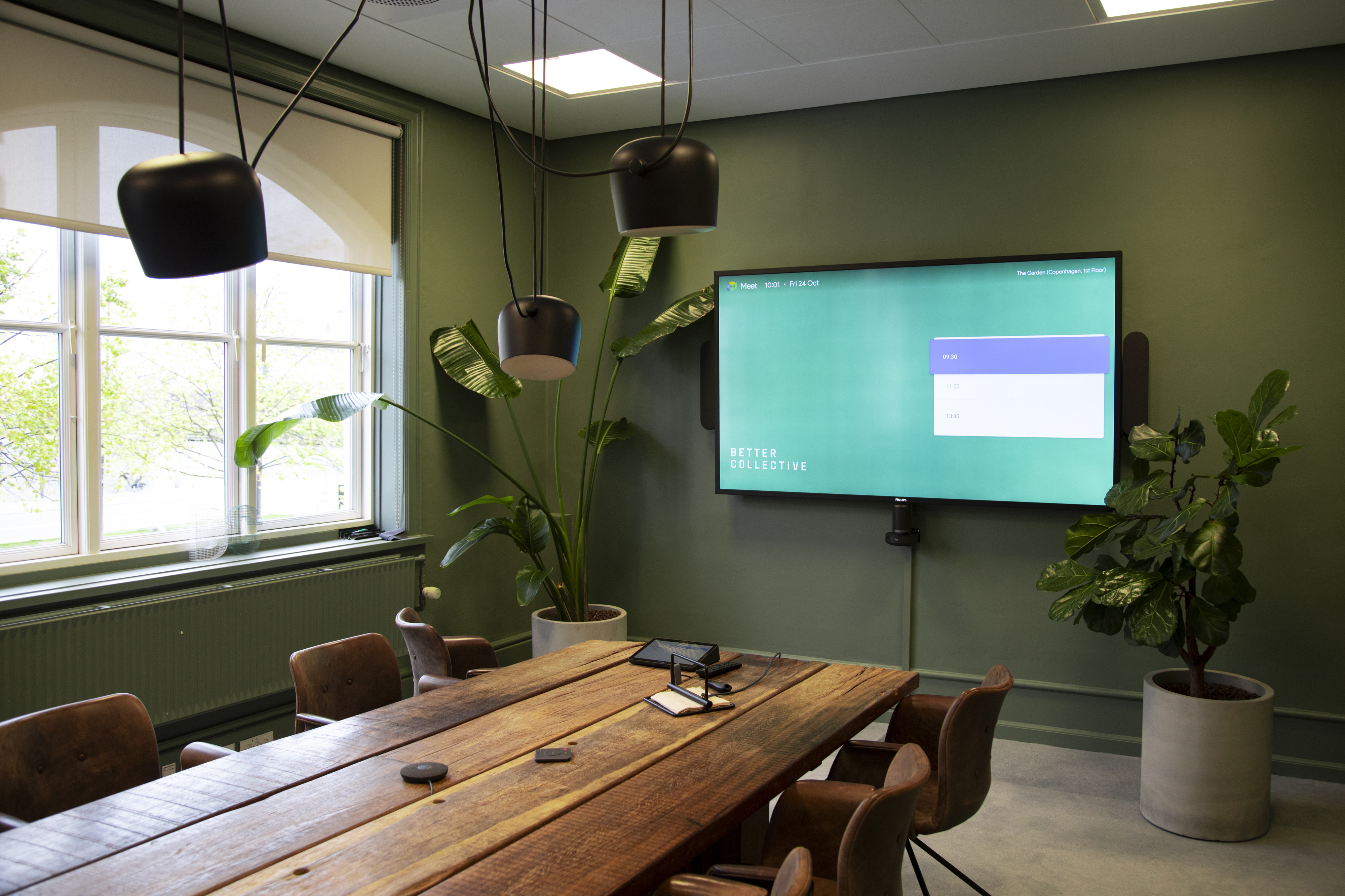 Modern meeting room with natural light, green walls and a large digital display.