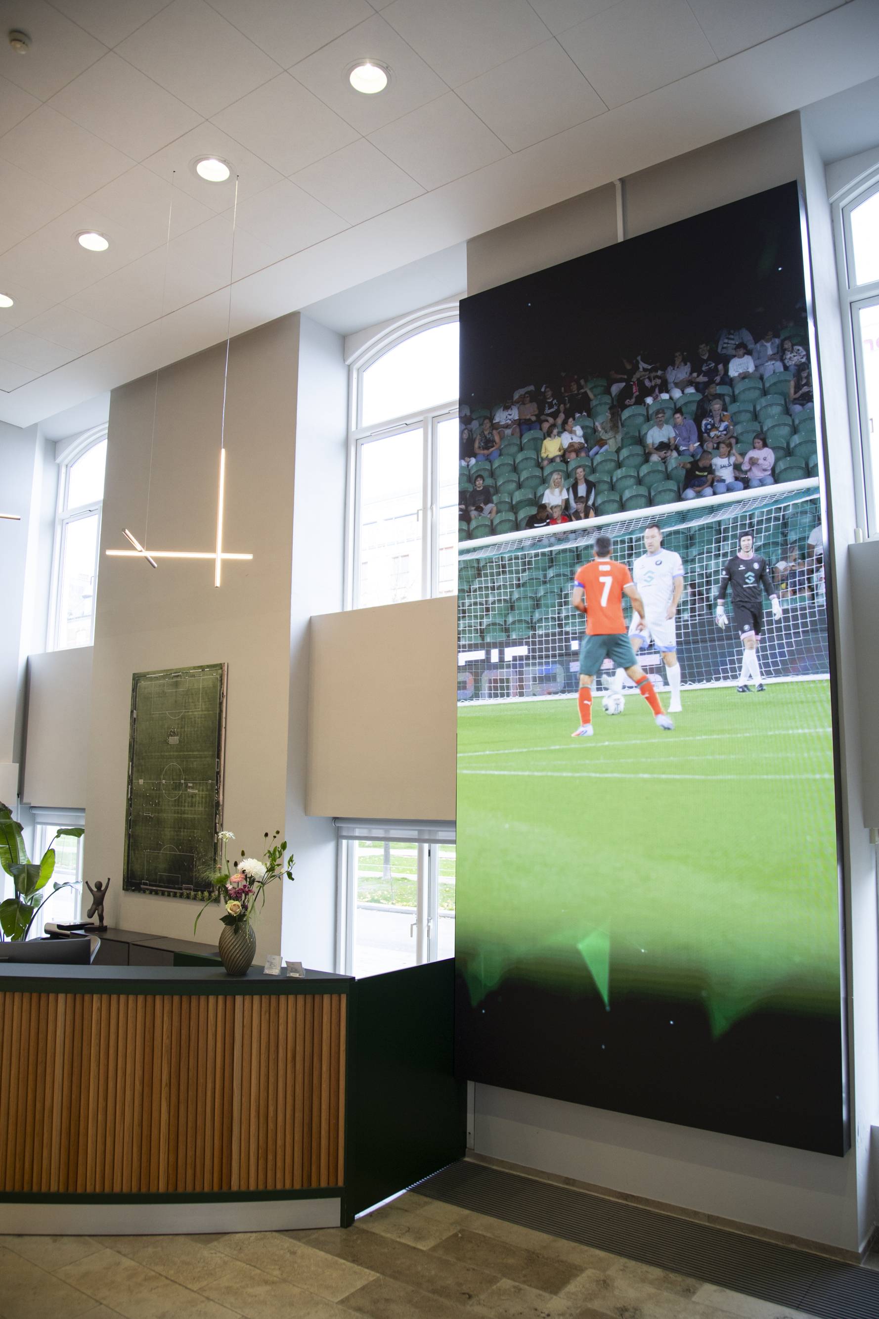 Modern office reception with a tall digital screen and bright natural light.