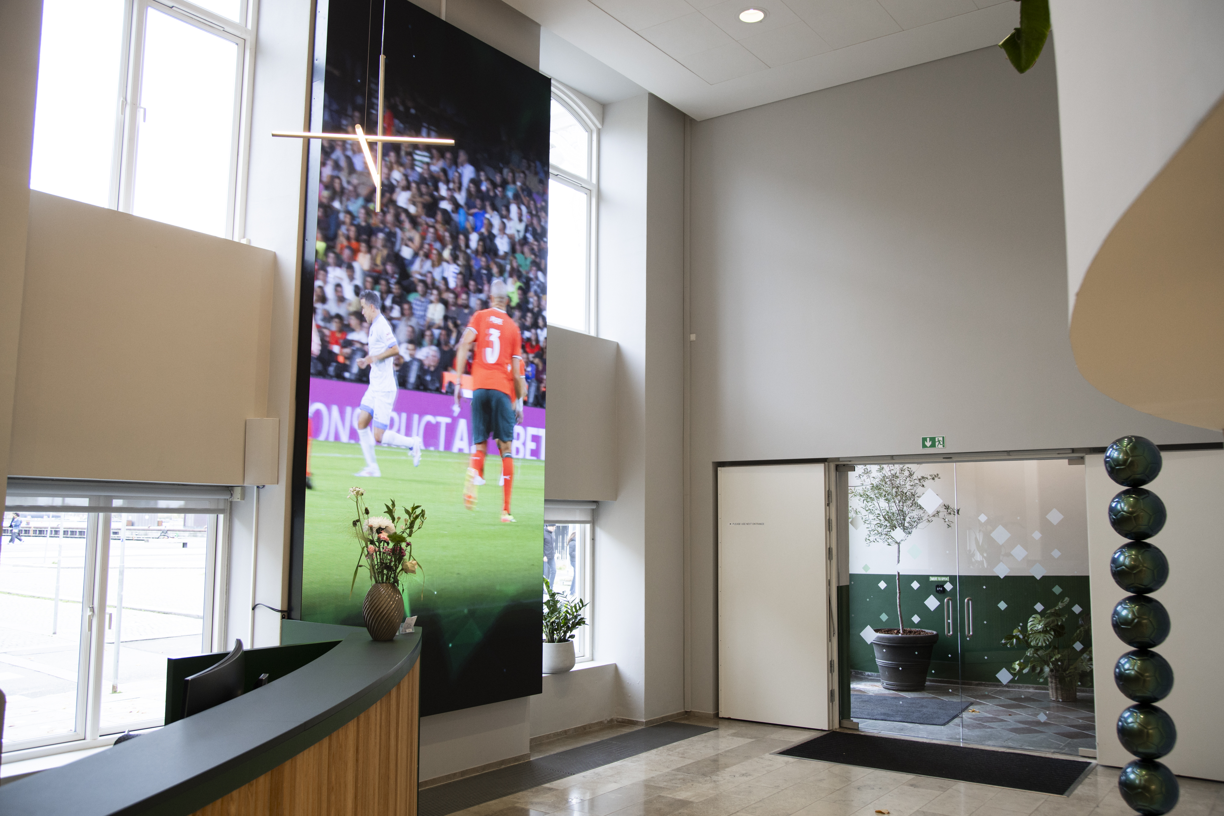 Bright office entrance featuring a tall digital screen and modern interior design.